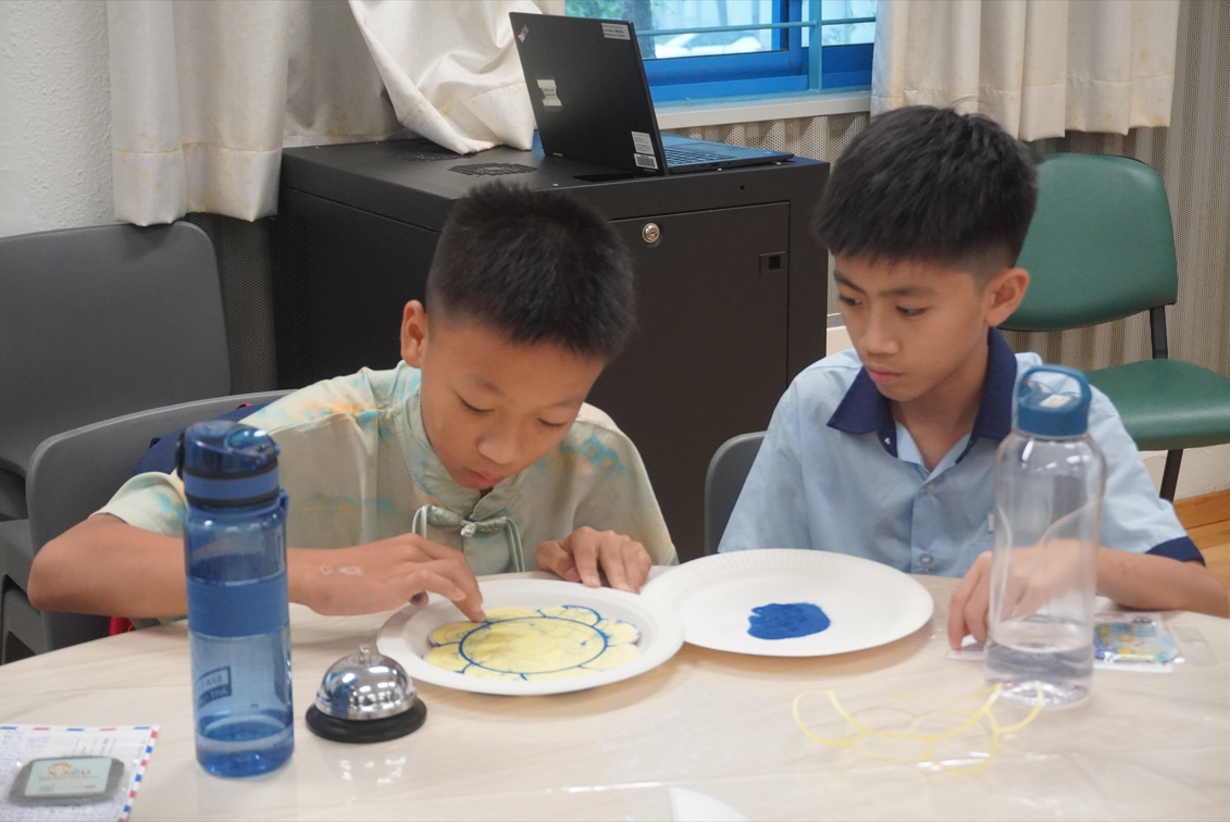 Two boys sitting at a table painting craft plates